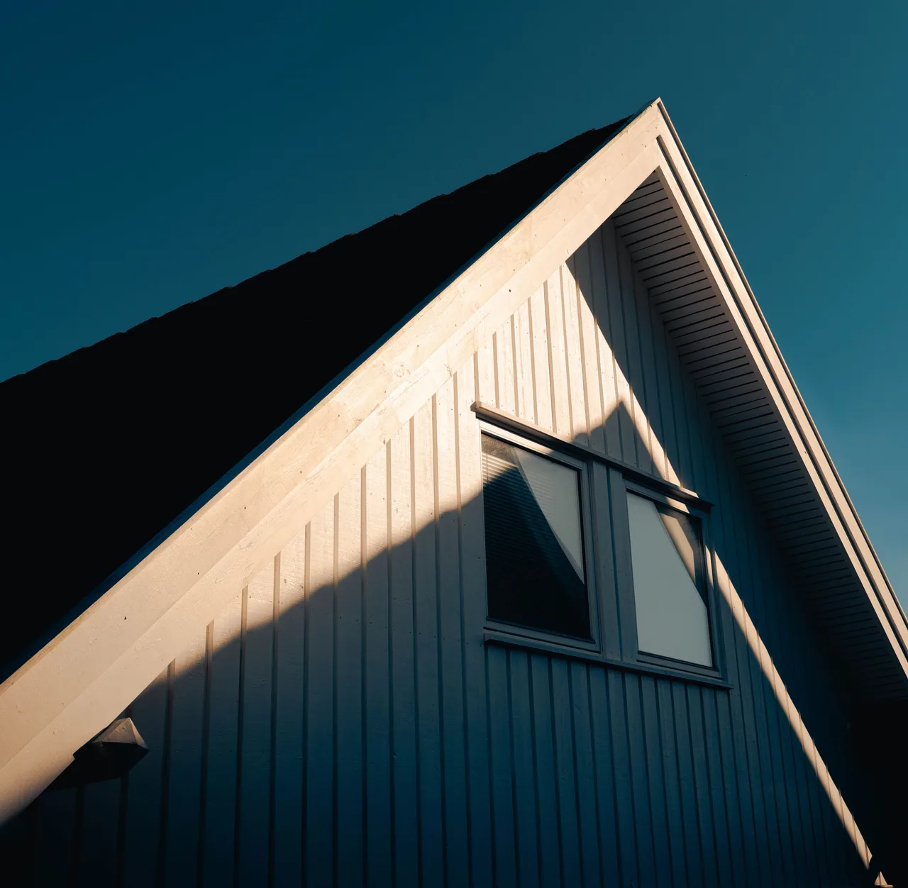 A steep gabled residential roof against a blue sky